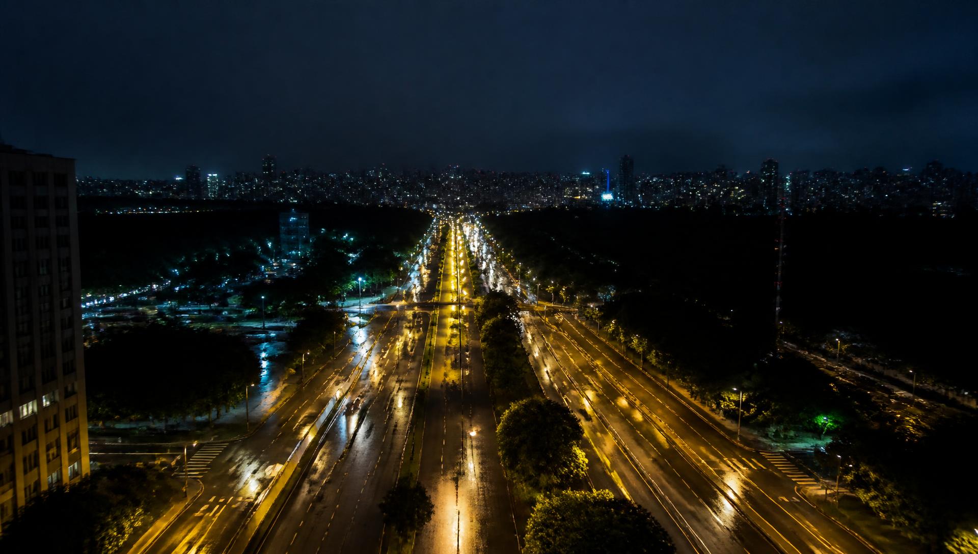 Avenida de uma cidade brasileira à noite iluminada por postes de iluminação pública