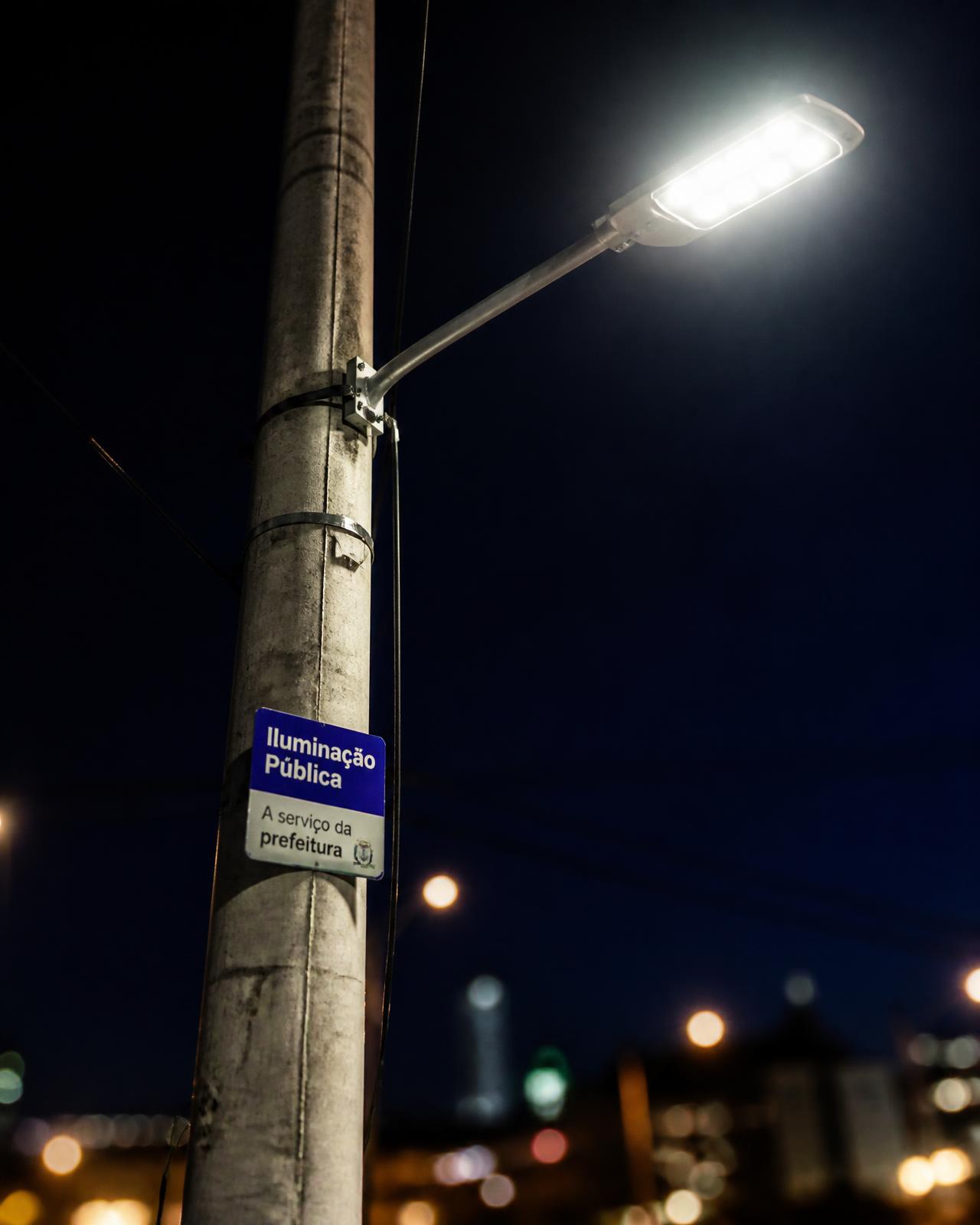 Poste de iluminação pública brasileiro com luminária LED acesa à noite